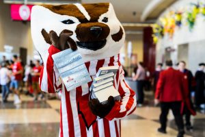 UW-Madison mascot Bucky Badger helps volunteers distribute complimentary copies of "The Death and Life of the Great Lakes" following the Chancellor's Convocation for New Students at the Kohl Center at the University of Wisconsin-Madison on Sept. 4, 2018. (Photo by Jeff Miller / UW-Madison)