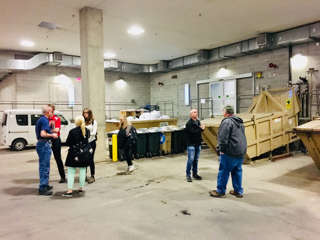 The Green Fund team assesses the cardboard collection area at Gordon Dining & Event Center. From left to right: Mark Mueller, Greg Heintz, and Breana Nehls from University Housing; Maddie Clarke and Meg DiPoto, the student applicants; a compactor vendor; and Lyle Jelle from UW Waste & Recycling.