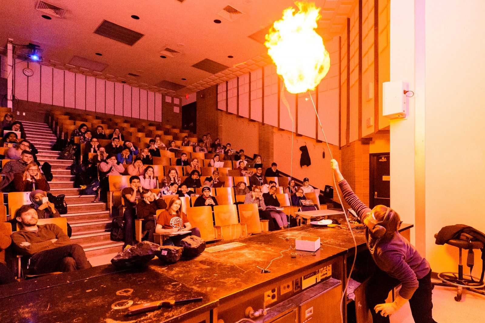 A woman stands at the front of a full lecture hall conducting a science experiment.