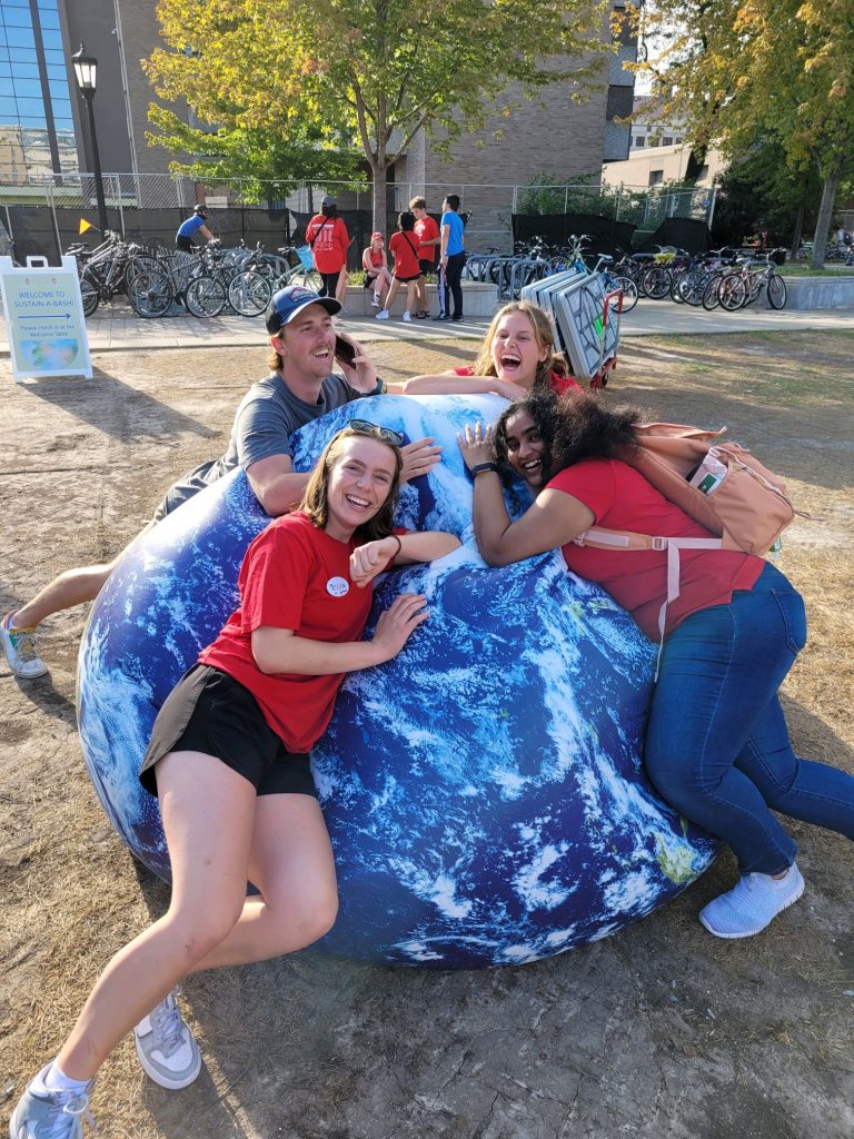 Four young women laughing and leaning against a large inflated earth