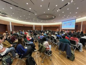Crowd of people in large circular room watching a presentation on a screen