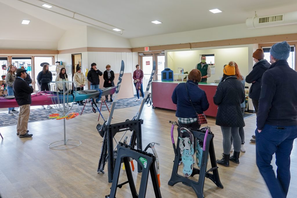 A loose circle of people in a large bright room with sports equipment on display