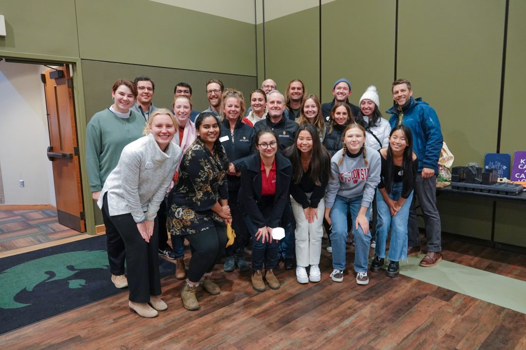 A dozen people posing in the corner of a room and smiling
