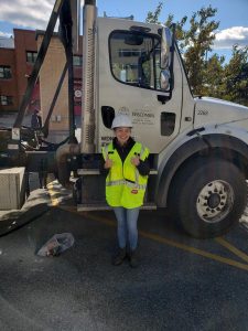 Morgan Barlin poses in front of a large white truck cab wearing a bright green construction vest.