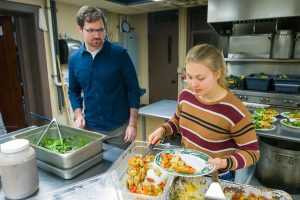 Two people serving food at a kitchen