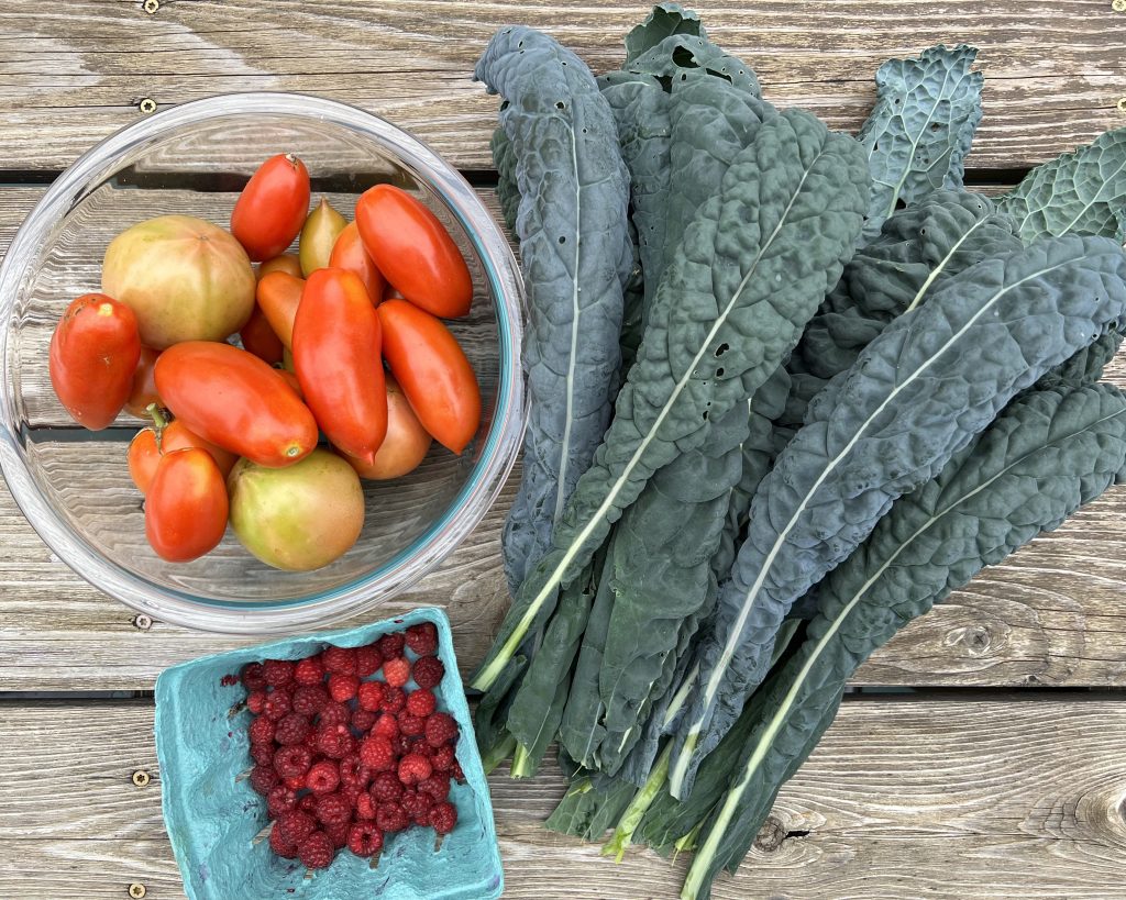 tomatoes, kale, and raspberries on a wooden surface
