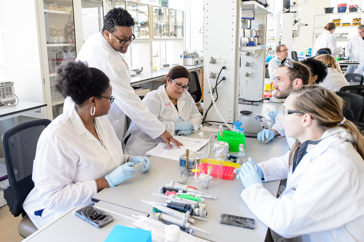 Many scientists in white lab coats and rubber globes surrounded by laboratory equipment