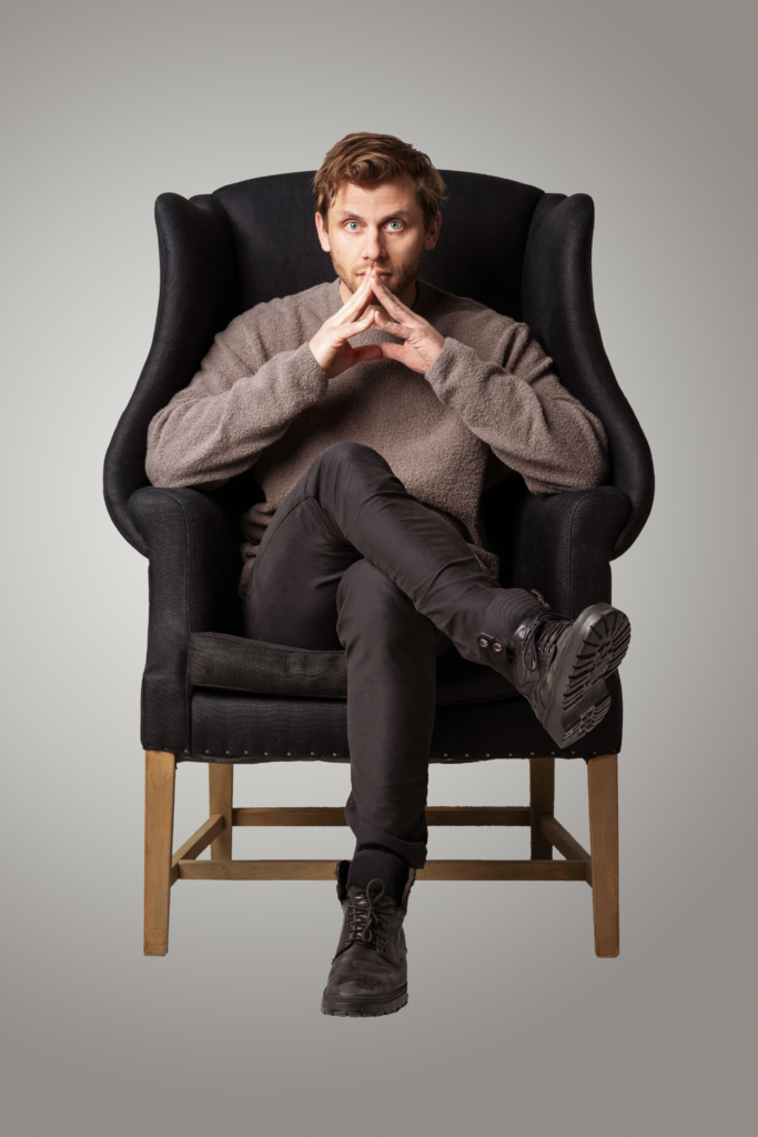 Charlie Berens sitting in a chair in front of a gray background