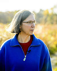 Karen Oberhauser in a blue jacket standing in front of a sunlit field
