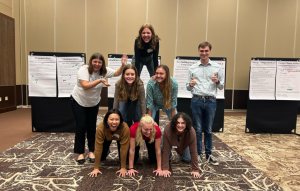 6 students form a pyramid in a conference room with 2 students standing next to them to spot