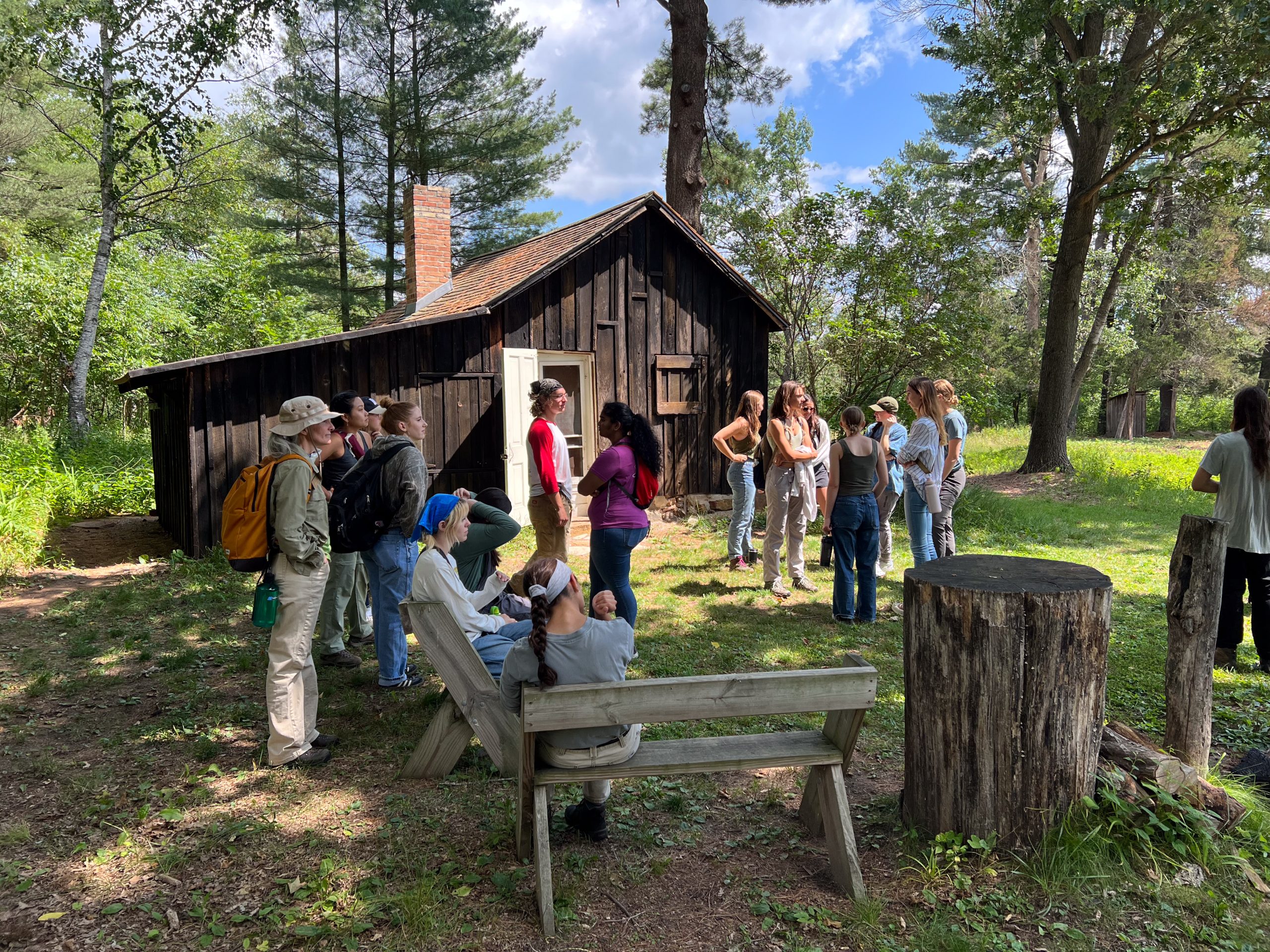 Students gather around a rebuilt chicken coop surrounded by pine trees.