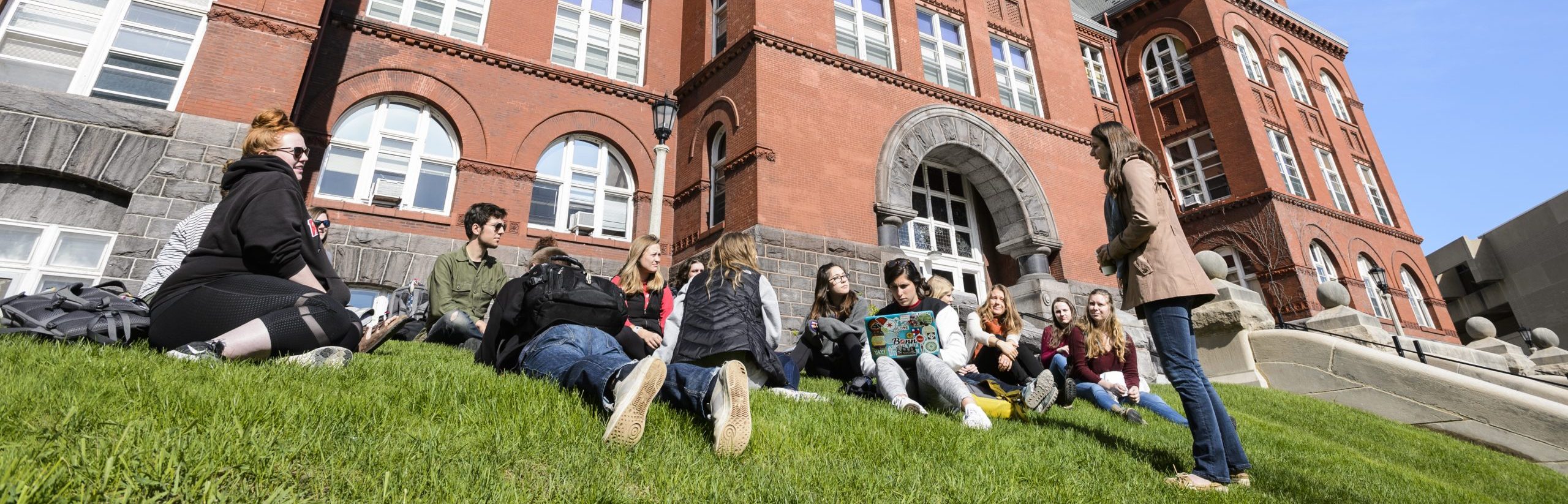 students sit on the grass outside science hall as their teaching assistant leads a discussion