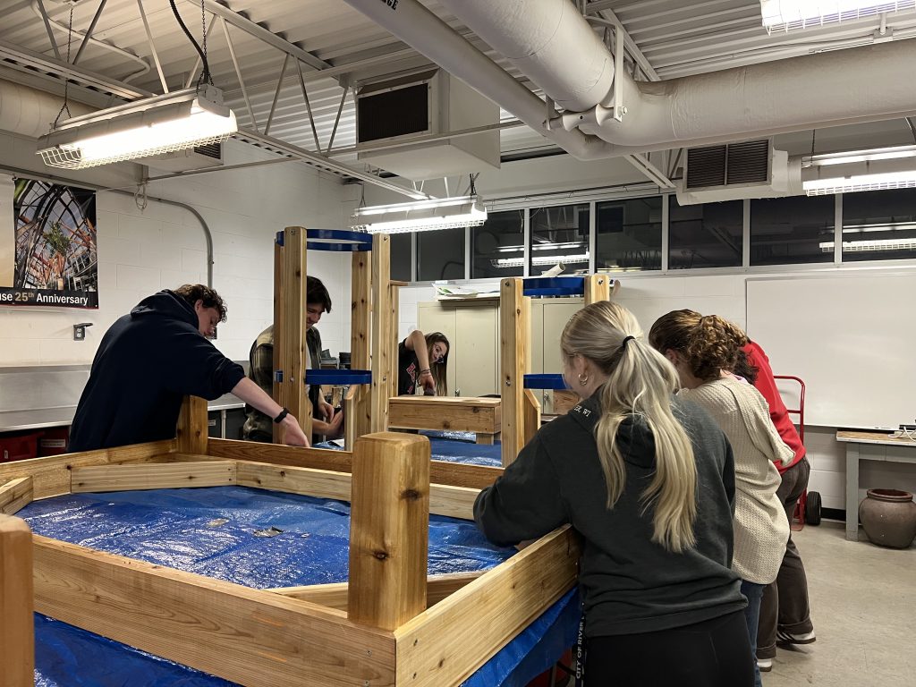The image shows 6 students building a structure made of wood and blue plastic for the aquaponics system.