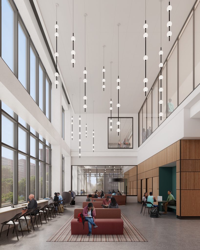 Tall atrium space with large windows to the left, hanging vertical lights and people sitting on chairs. 