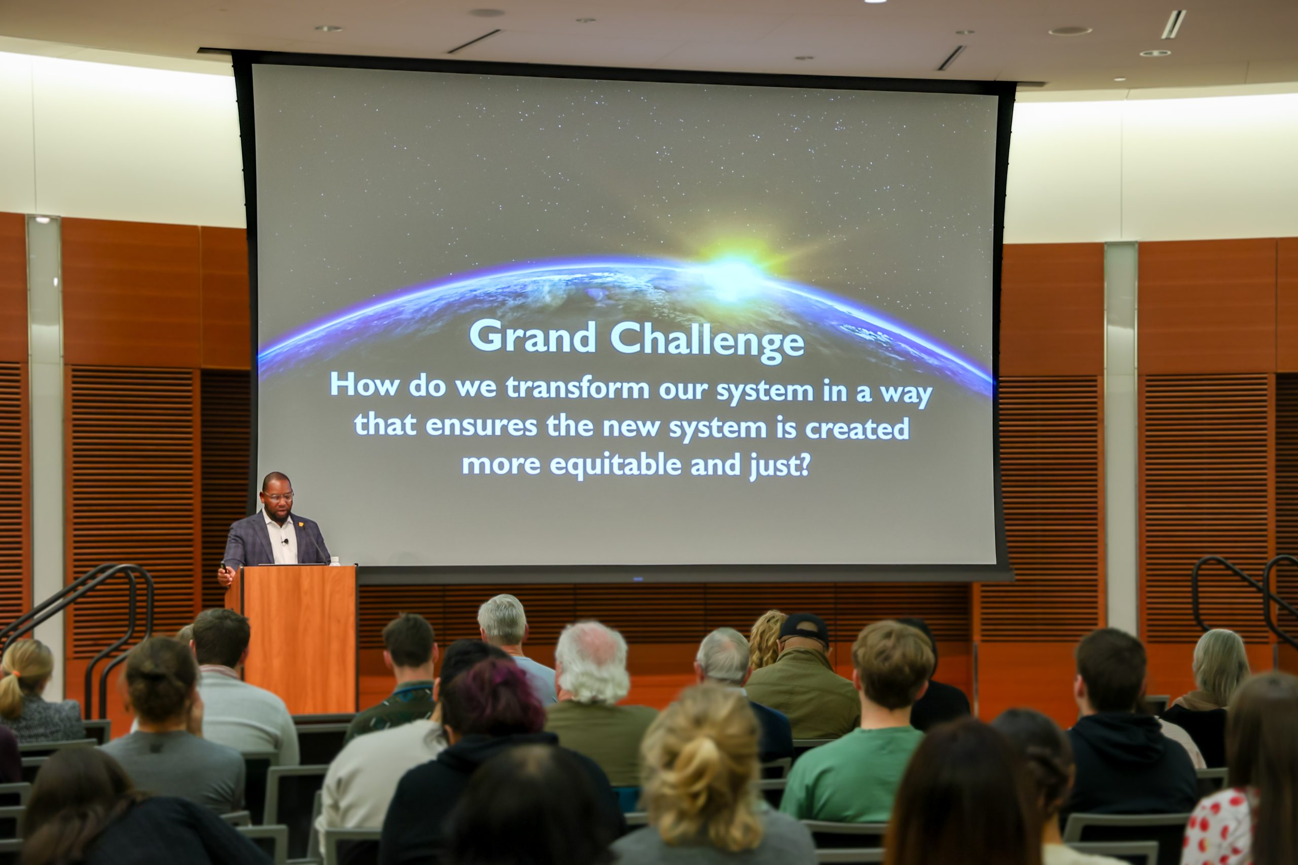 A man stands at a podium in a full auditorium. 