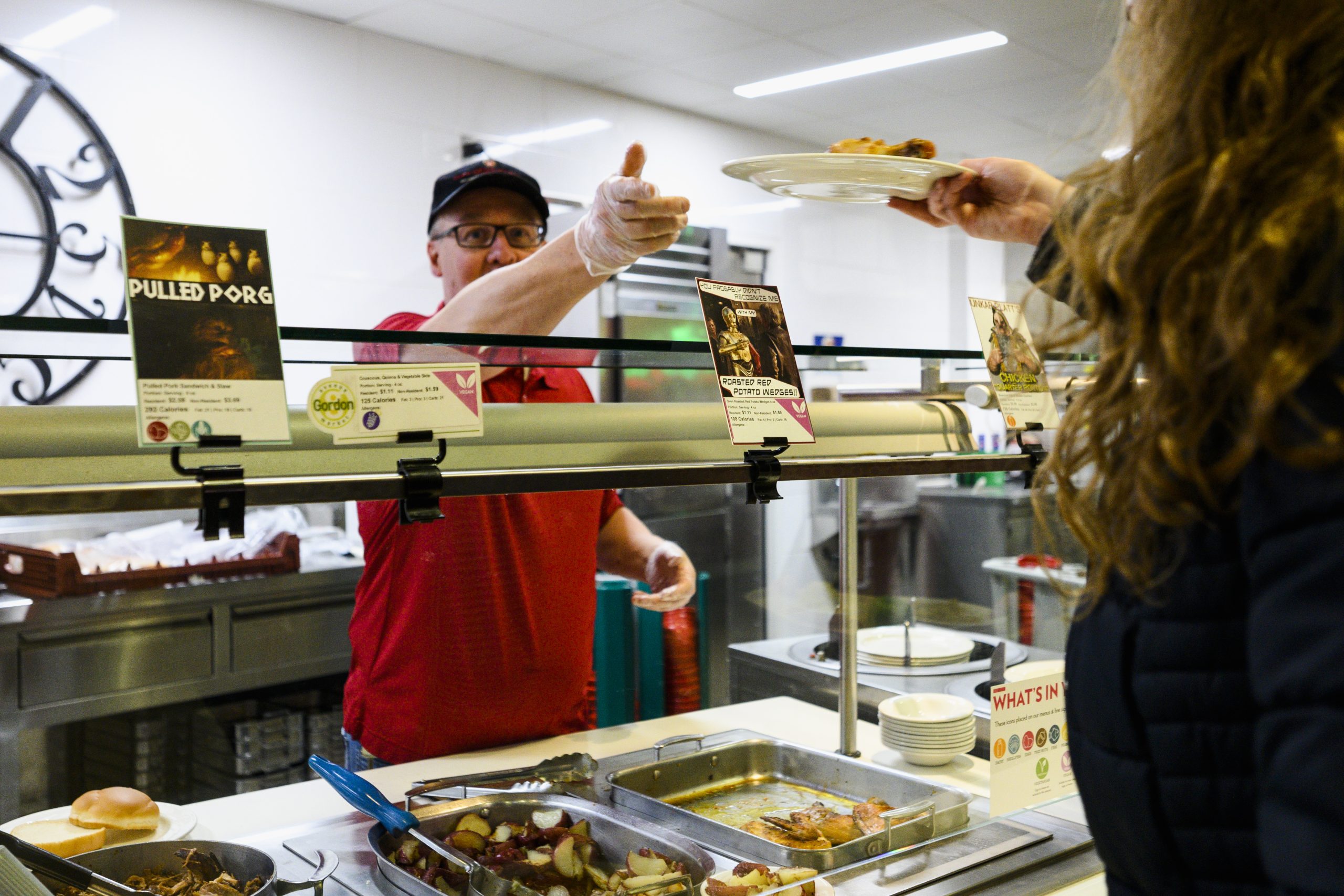 A Housing Staff member passes a plate of chicken over the serving counter to a student with signs featuring a Star Wars themed menu.