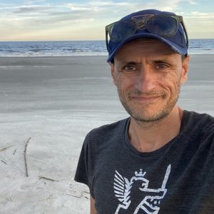 Claudio Gratton standing on a beach with water in the distance