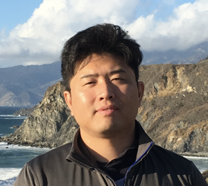Feng He standing in front of a dramatic coastal cliff with puffy clouds above