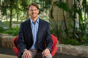 Gregory Nemet professional headshot sitting in a red chair with trees in the background