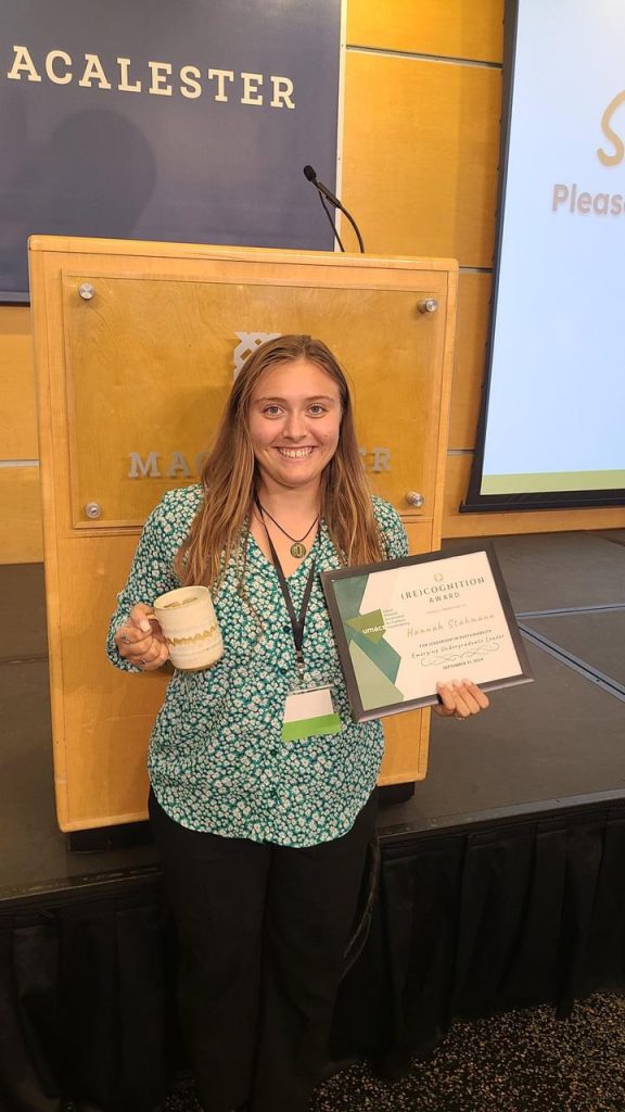 Hannah Stahmann holding a plaque and smiling in front of a podium.
