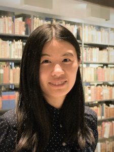 Headshot of Mohan Qin in front of a bookcase full of books. 