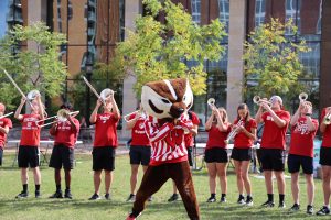 Bucky dances in front of members of the UW marching band as they play their instruments dressed in red