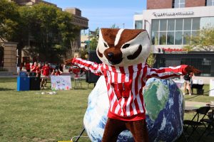 Bucky stands with his arms outstretched in front of a blow-up Earth