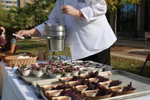 Chef plates food into containers, including soup, chips, and a salad