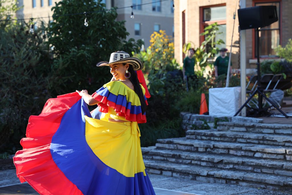 A Colombian dancer in a cowboy hat and long yellow, red, and blue dress twirls her skirt