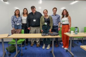 Six people stand side-by-side at the front of a classroom, smiling.