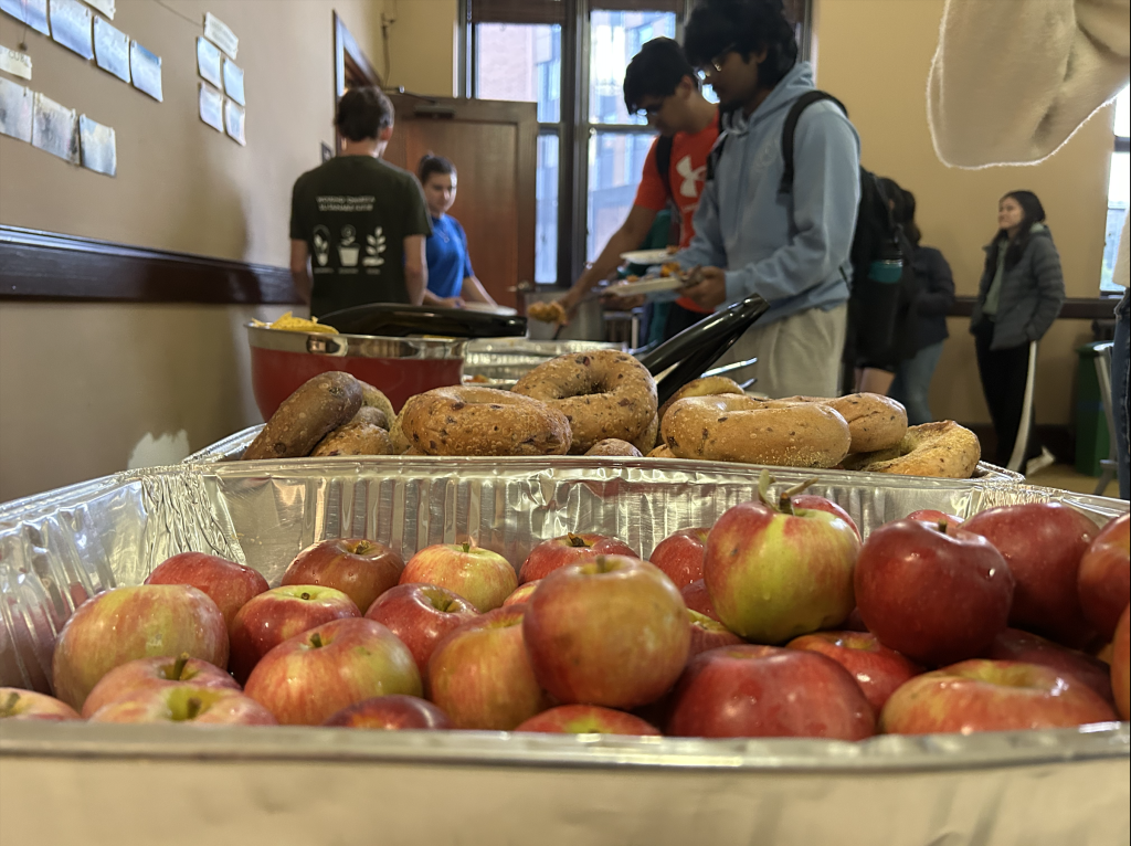 bin of apples with a bin of bagels and people standing in the background