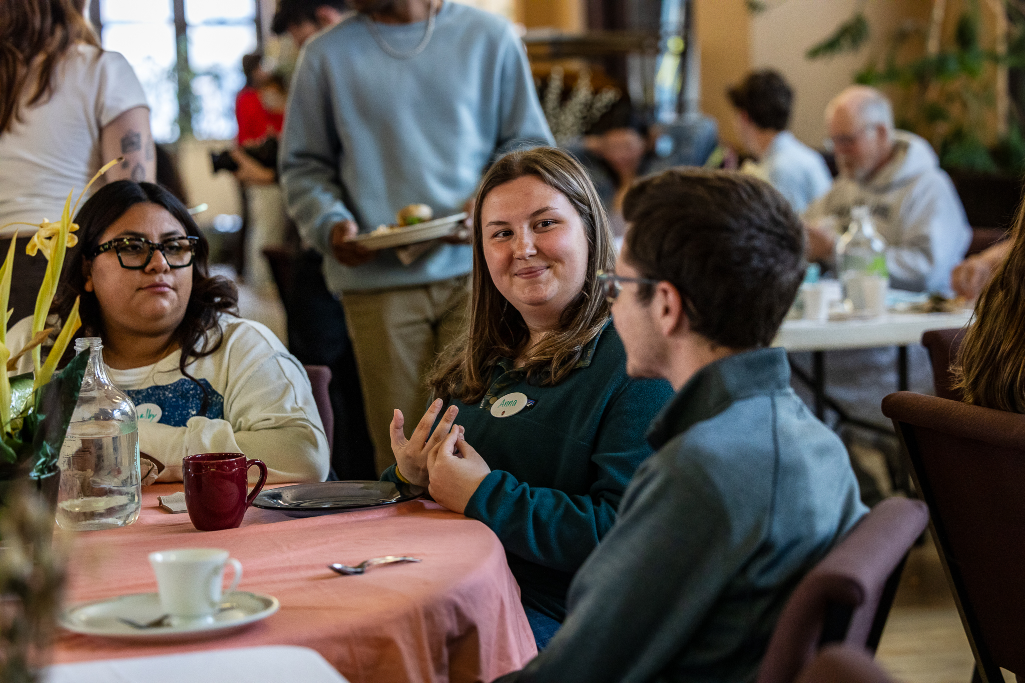 Three students sit around a roundtable smiling and talking.