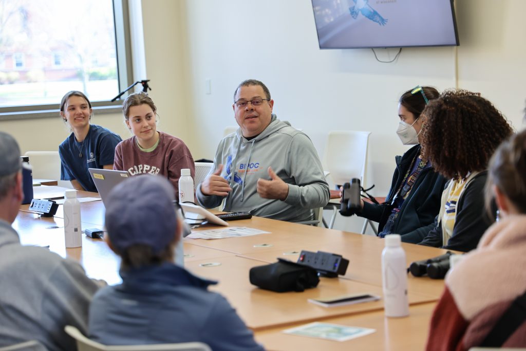 Group of student interns and members of the BIPOC birding club sit and talk around a table.
