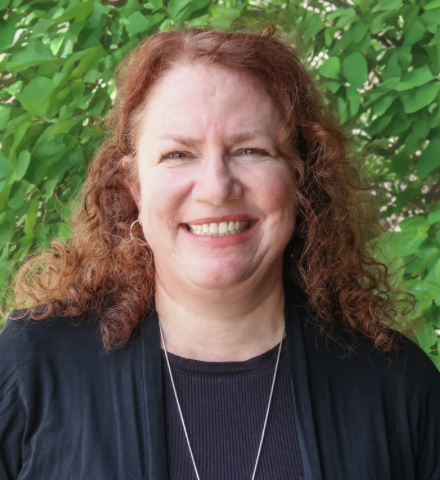 Kim Wahl in a black shirt standing in front of a green background.