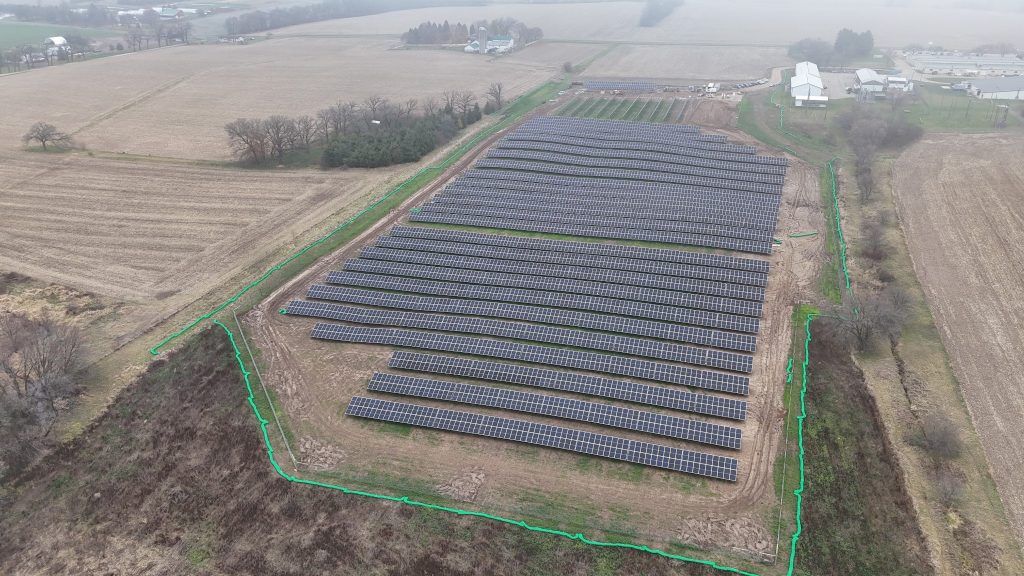 Rows of black solar panels in a brown field from an elevated viewpoint.