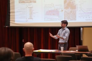 Luca Mastropasqua speaks to attendees during the RISE–EARTH: Technology session at the fall 2024 Sustainability Research Visioning Event. He stands in front of a projection screen with technical diagrams, gesturing mid-presentation. A table with notes and a laptop is in front of him, with audience members visible in the foreground.