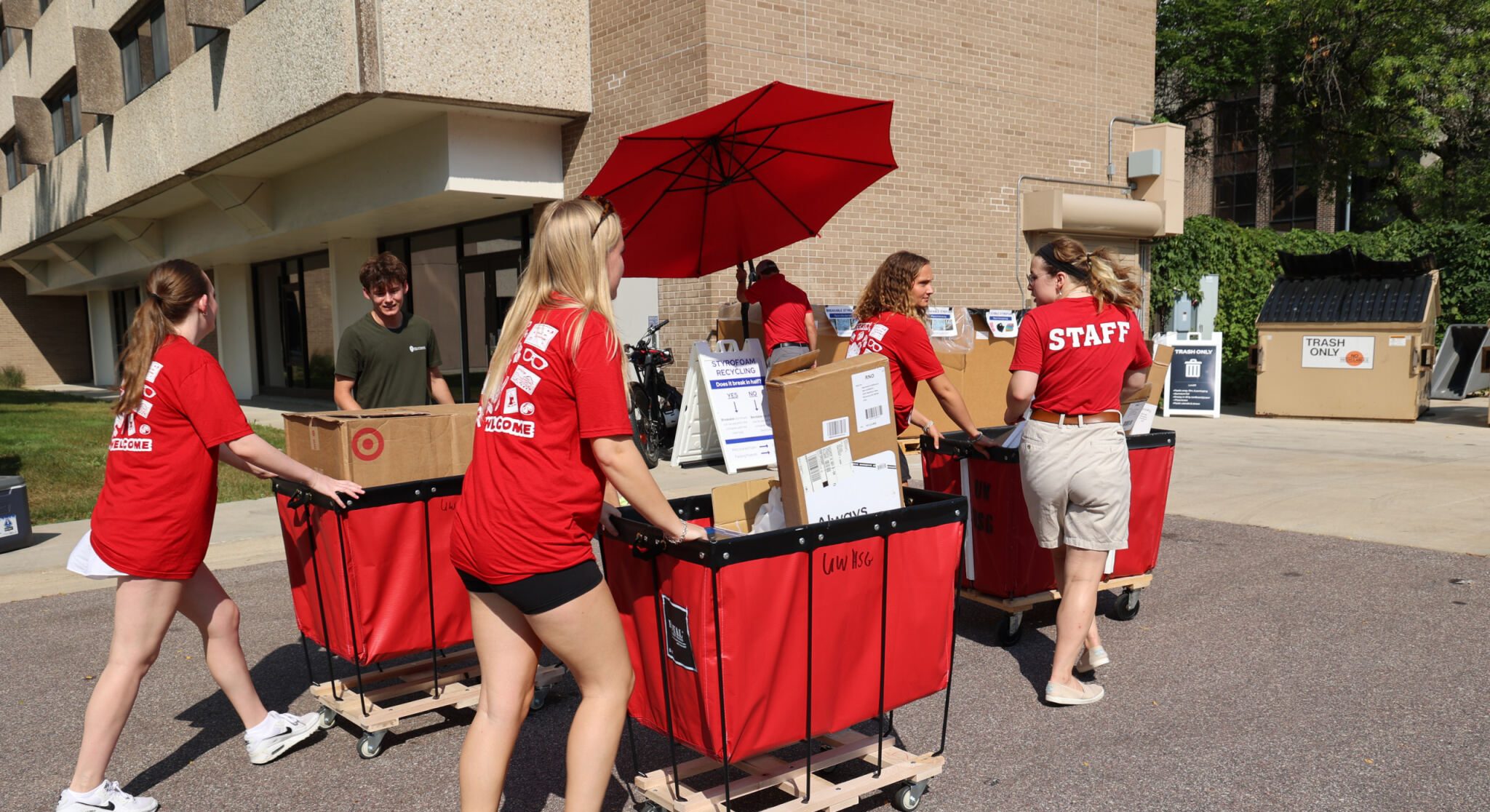 A group of students push Housing's red rolling carts filled with boxes outside of a residence hall.