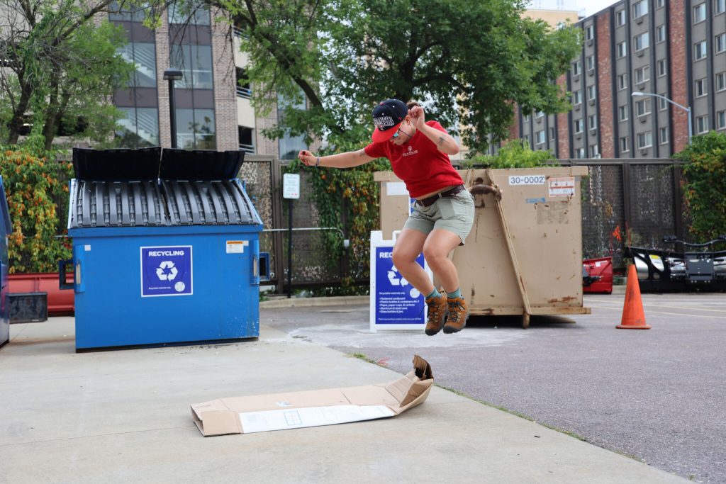 Student is mid-jump as she tries to flatten a cardboard box.