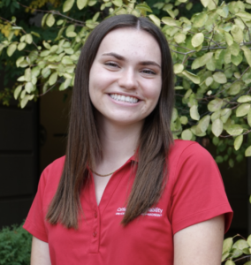 Olivia in red shirt in front of greenery