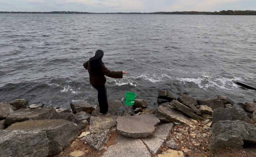 A student throwing a green bucket into the lake to sample water