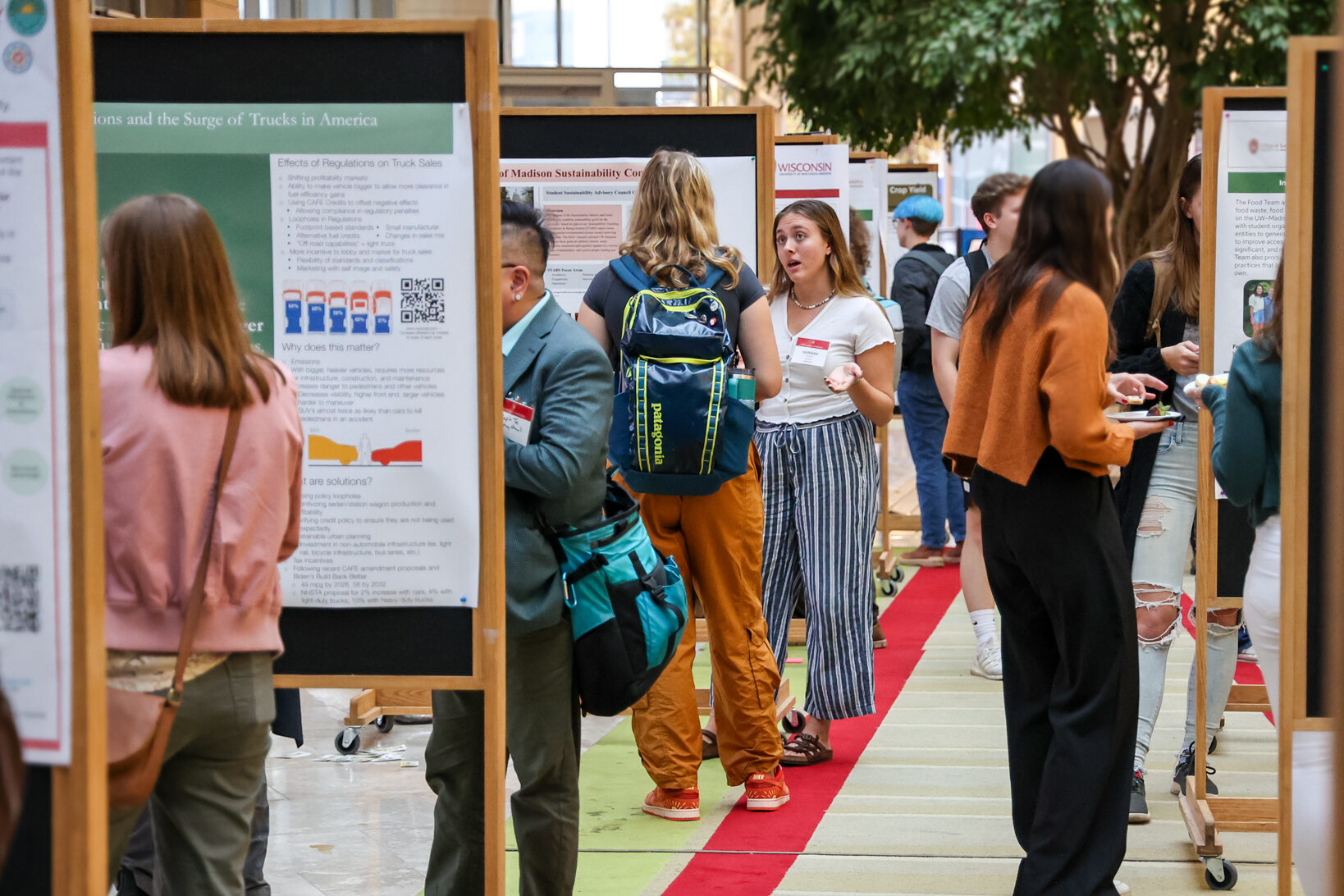 Attendees talk among rows of research posters during the Sustainability Symposium, with presenters and guests gathered in a bright indoor event space.