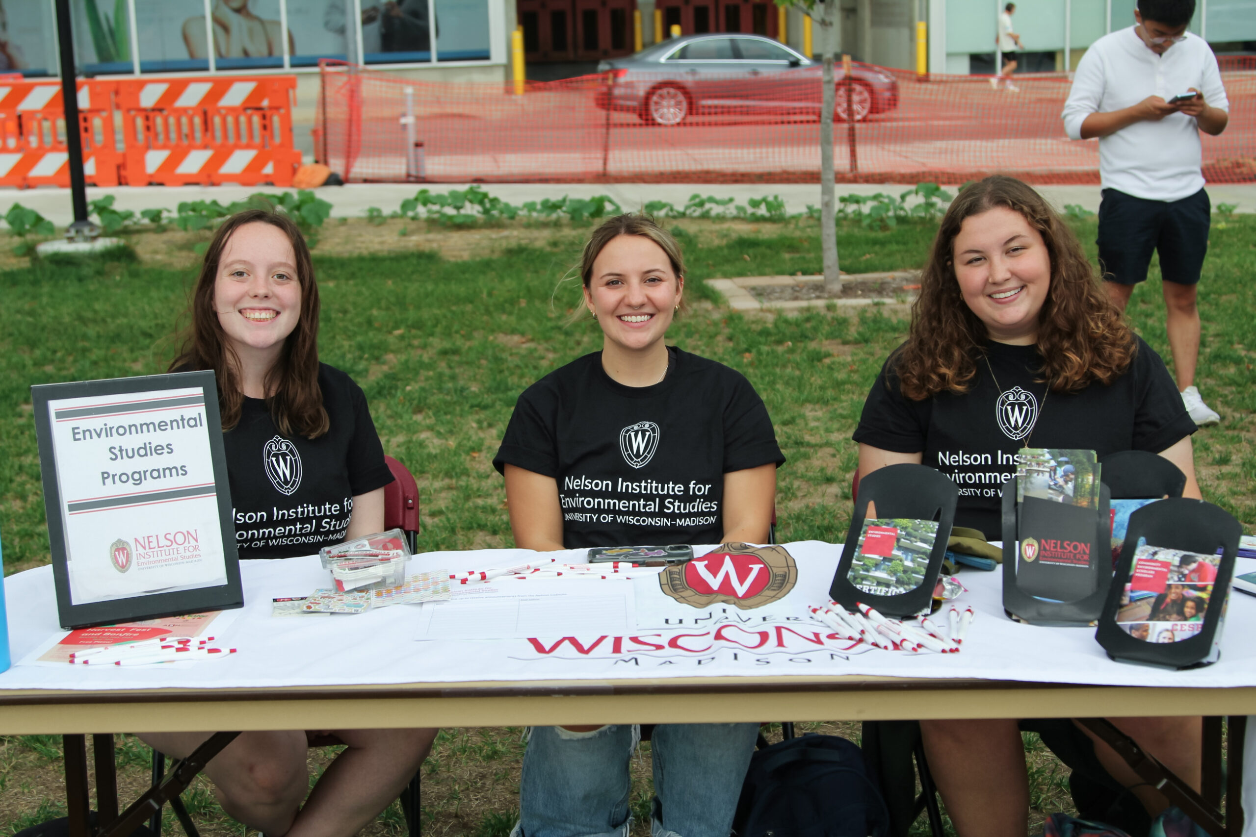 Three Nelson Ambassadors sit side-by-side at a table covered in outreach materials.