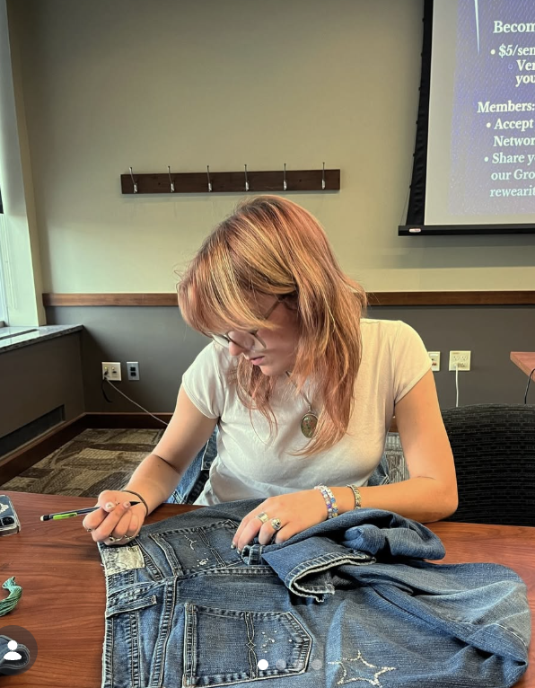 A student is looking at a pair of jeans and embellishing them during a Re-Wear It workshop. The jeans already have some jewels in the shape of stars.