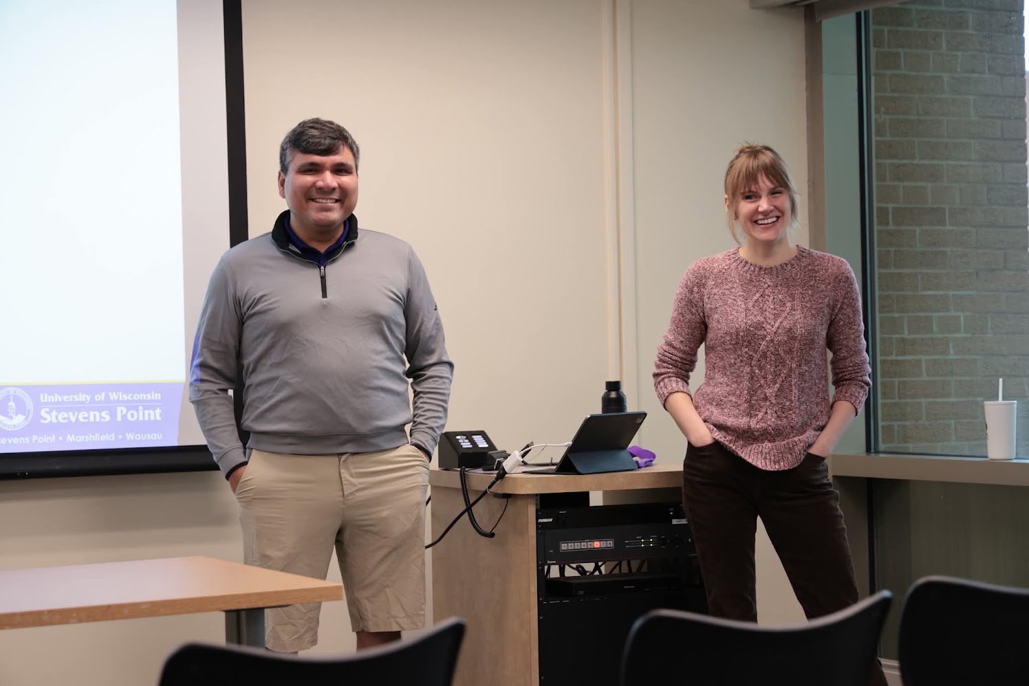 Michelle Gullickson stands next to her colleague, in the front of a classroom. She is smiling and presenting.