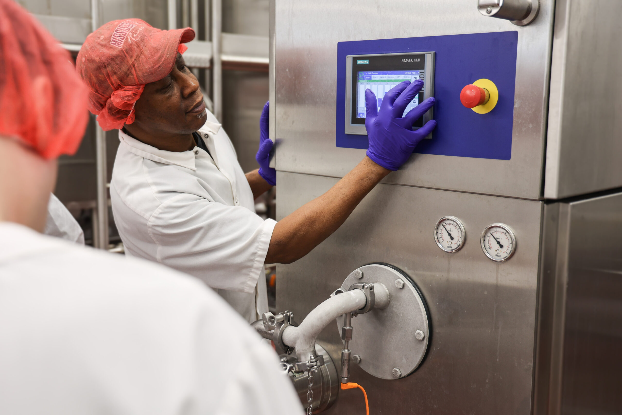 A person wearing a red hairnet and purple gloves operates a touchscreen on an industrial freezer.