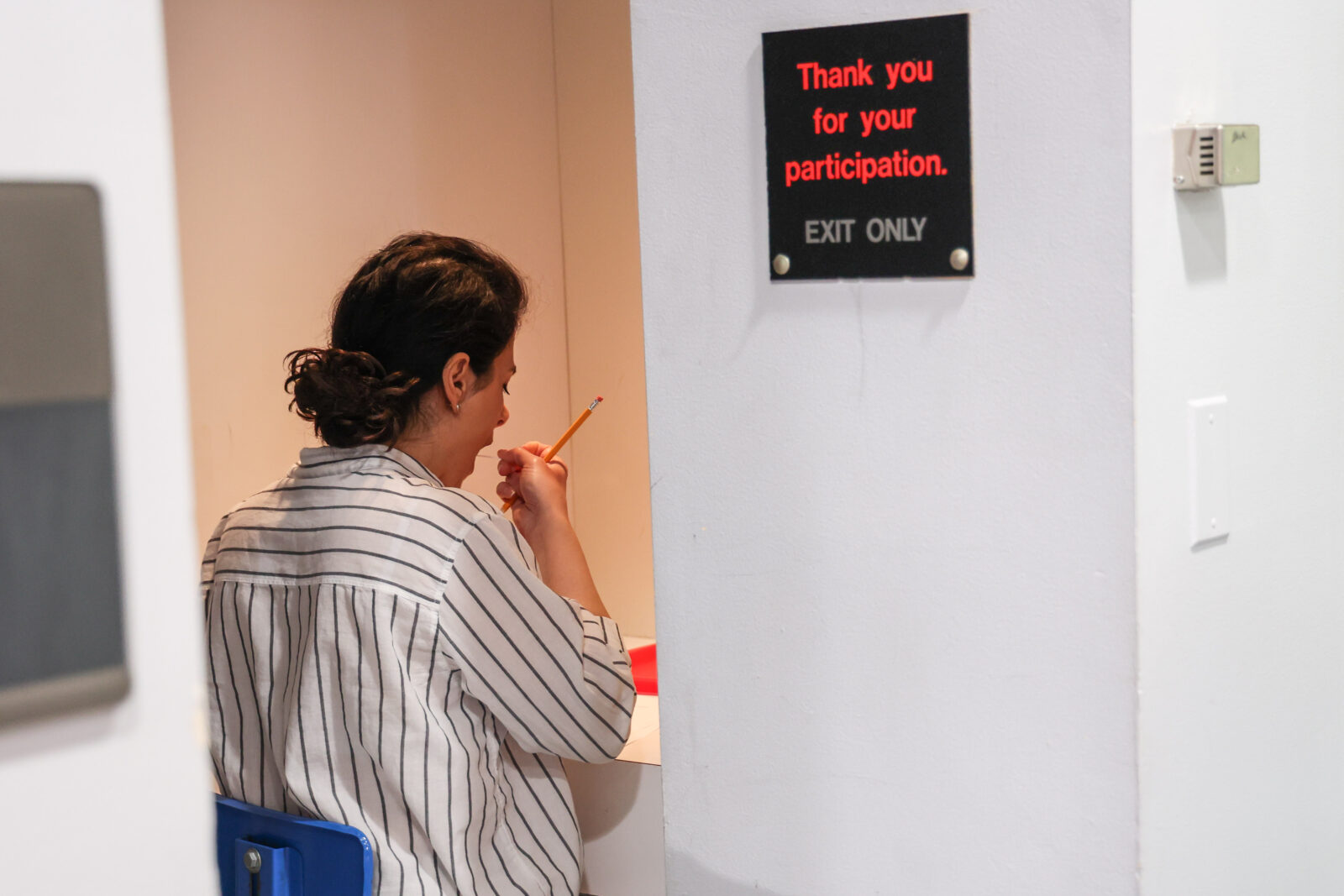 A woman in a striped shirt takes a bite of ice cream in an individual sensory testing booth at Babcock Hall. A sign above her reads “Thank you for your participation. Exit only.”
